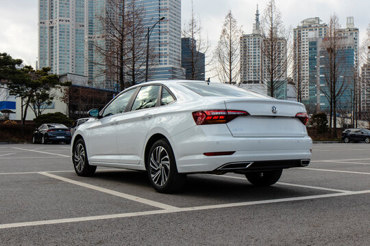 January 31, 2021, Seoul, South Korea - A white Volkswagen Jetta sedan parked in an outdoor parking lot with a city skyline in the background.