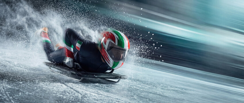 Skeleton athlete with an Italian helmet speeding down an ice track. Dynamic winter sport action shot with high-speed motion blur and flying ice spray for the 2026 games concept.