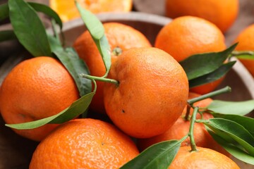 Fresh tangerines and green leaves in bowl on table, closeup