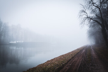 Foggy Mittellandkanal in Bramsche with riverside path and trees, cold wet winter mood and wide...