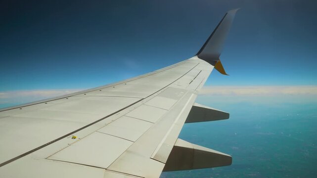 Airplane wing flying above ground, flaps ailerons winglet over haze and plains. Aircraft wing gliding over earth, spoilers wingtip over blue horizon. Jet wing cruising through sky, metal surface flaps