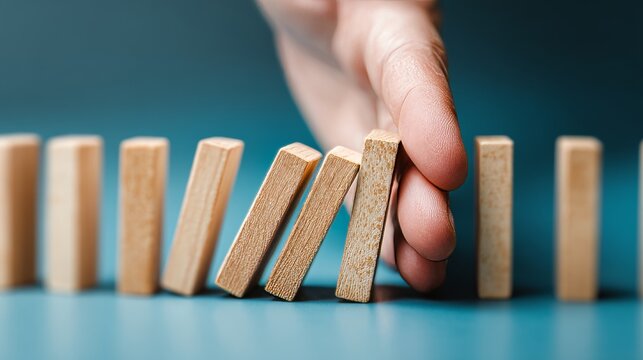Human Hand Interrupting Falling Dominoes on Blue Surface Symbolizing Prevention, Control, Risk Management, and Cause-and-Effect Intervention