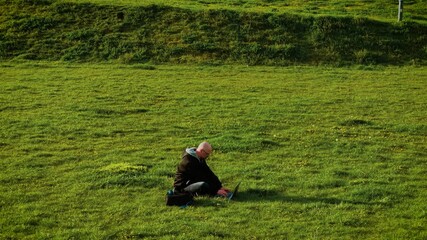 Man working online typing browsing products in internet store. Freelancer searching items on e-commerce website while sitting on grass. Remote shopper using laptop outdoors to explore digital