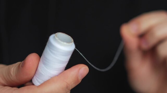A seamstress holds a roll of white thread.
Sewing clothes with thread.
Thread for sewing and mending clothes.
A white skein of thread.