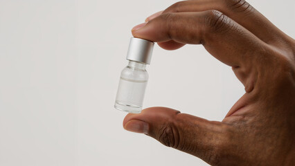 African American Hand Holding Small Glass Vial, Skincare Cosmetics Product on Solid Background