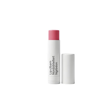Close up of a white tube of pink tinted lip balm on a black background