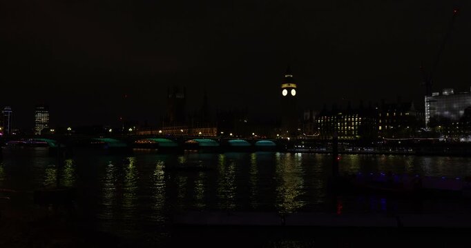 Red buses, traffic and people on Westminster Bridge over the River Thames at night, next to Big Ben and The Houses of Parliament, London, England
