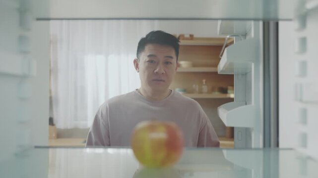 Inside view of man retrieving apple, Intimate moment in contemporary kitchen as man selects apple from shelf