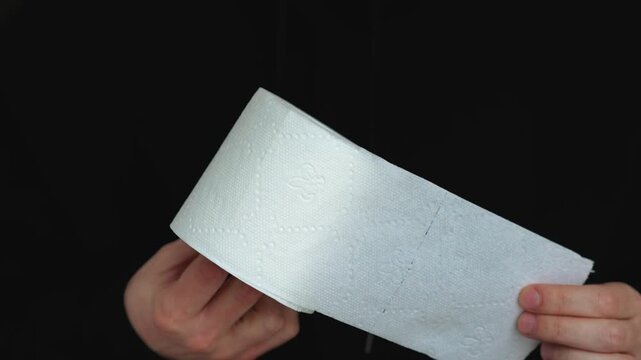 A man tears a piece of toilet paper from a roll while sitting on the toilet.
Toilet paper in a man's hands.
A man defecating in the toilet and a white roll of toilet paper.
Hygiene, toilet, toilet, cl