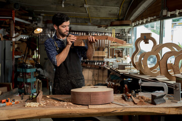 Luthier inspecting guitar neck blank in workshop, craftsman building acoustic instrument