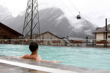 Kid in outdoor swimming pool looking at mountain gondola lift © Arkady Chubykin