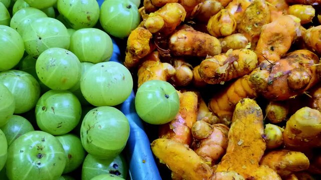 A tight close-up of fresh green amla (Indian gooseberries) piled in a market tray, with turmeric roots visible along the edge.