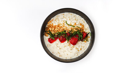 Top view of healthy oatmeal porridge with fresh strawberries, granola, and mint in a black bowl