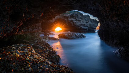 Sunset sea cave arch with glowing sunstar and smooth water reflecting warm light