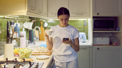 Woman checking smartphone while holding cup in cozy home kitchen. Concept of promotional content for app marketing, web banners, landing pages and digital product advertising.
