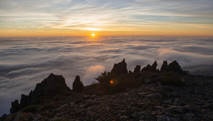 Obraz premium Sunrise above layered cloud sea with jagged mountain ridge and warm light