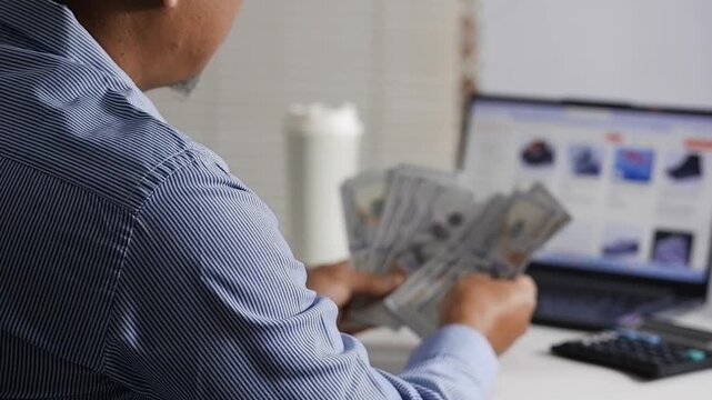 A man searches for price references online while counting dollar bills in front of his laptop and holding his forehead because he doesn't have enough money. Calculating the estimated cost.