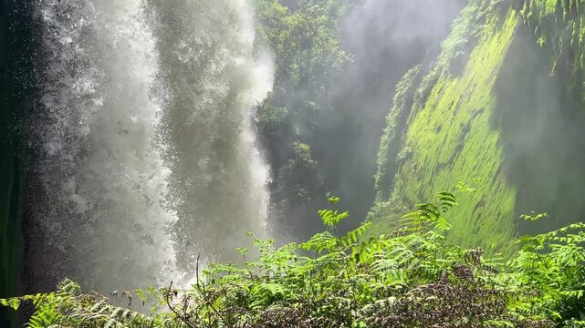Blawan Waterfall around the Kawa Ijen Crater, hidden in the tropical jungle, East Java, Indonesia. A picturesque view of a powerful waterfall surrounded by sharp rocks covered with moss and plants. 4К