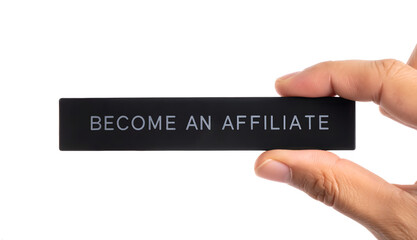 Close-up shot of two fingers holding a long black acrylic plate with white engraved text “become an affiliate”, isolated on a clean background
