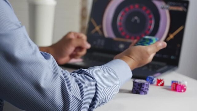 Excited overjoyed man at computer desk holding online casino poker chips, jetons, winner feeling euphoric with bet gambling victory, looks at screen celebrates fantastic news, received best prize