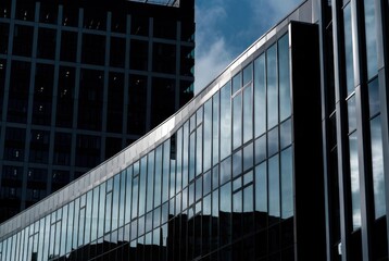 Architectural detail of a modern business center with a curved glass facade reflecting the sky. Contemporary office buildings with sleek glass and steel structures in a financial district.