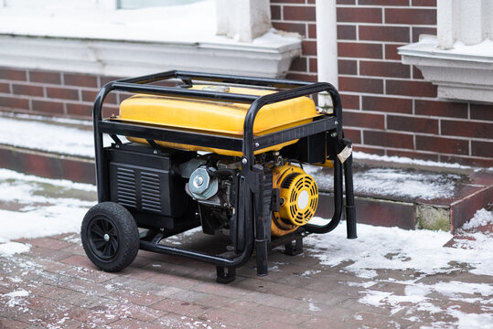 Yellow portable gasoline generator on wheels standing on a snowy sidewalk. Industrial backup power source for home or business during winter blackouts.