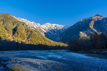 Beautiful mountains and the Azusa River of Kamikochi National Park glowing in the morning sunlight during autumn in Nagano, Japan.