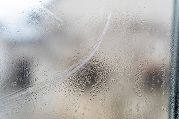 Close-up view of a fogged window with condensation, creating an abstract design. The blurred background hints at an interior space, illustrating a moment of stillness and reflection.