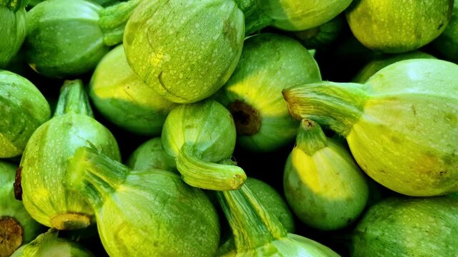 Fresh tinde vegetables piled at a market stall show plump green bodies, short stems, and smooth skins, captured in daylight inside a vegetable shop.