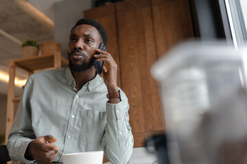 African American man talking on a smartphone while sitting at a table at home, gesturing during a business call, remote work communication, problem solving, and professional discussion