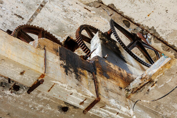 A rusty old machine with three gears. The machine is old and has been exposed to the elements for a long time. Scene is one of decay and neglect, as the machine has clearly seen better days