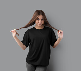 Template of stylish black oversized t-shirt on posing girl in gray jeans, front view, for design, branding.