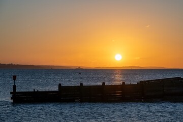 Fototapeta premium sea defence at Hill Head Hampshire England with bright orange sky at sunset over The sea and The Isle of Wight in the background