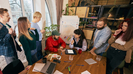 Startup coworkers analyzing strategy around conference table. Concept of business planning, teamwork dynamics, collaborative decision making and corporate growth.