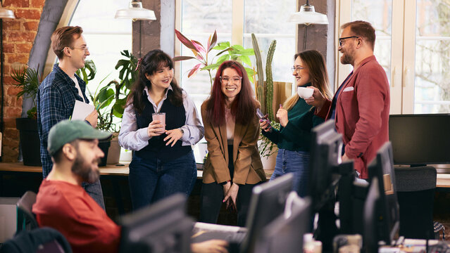 Informal office meeting with diverse team in modern workspace. Concept of inclusive modern office, cross functional collaboration, internal communication, team alignment.