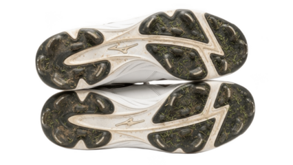 Pair of white baseball or softball cleats shown sole up with dirt covered molded studs, authentic game worn footwear highlighting traction pattern and real field use on grass and clay

