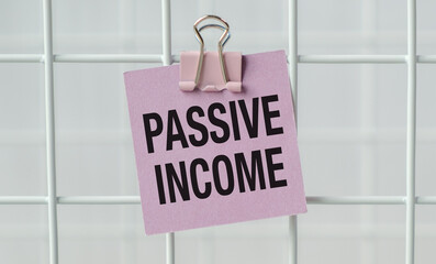 A pink piece of paper with the words PASSIVE INCOME written on it. The paper is clipped to a white...