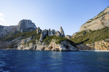 Picturesque rocky coast, cliffs with caves in the morning light, L'Aguglia rock peak, blue sea and Cala Goloritzé beach, Golfo di Orosei, Baunei, Sardinia, Italy