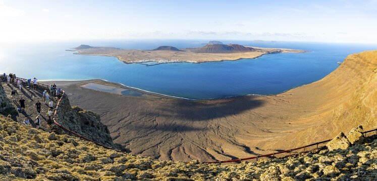View of La Graciosa island with volcanic craters in the evening light, tourists on an observation deck at the Mirador del R&iacute;o viewpoint designed by artist C&eacute;sar Manrique, Lanzarote, Canary Islands, Spain