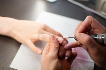 A nail technician removes gel polish from a clients nails using an electric nail drill