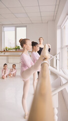 Side view of young ballet student practicing leg extension at barre. Concept of dance studio advertisement, classical ballet promo visuals, children activity marketing, and training program promotion. © master1305