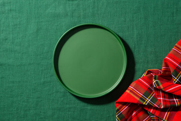 Elegant green plate on textured tablecloth, vibrant plaid napkin, minimalist food styling setup. Green background. Close up. Top view.