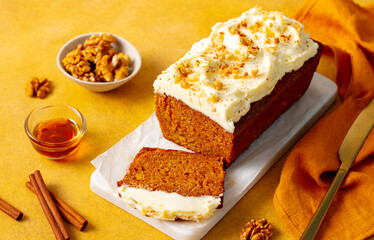 Carrot cake loaf on a white marble serving board. Yellow background. Close up.