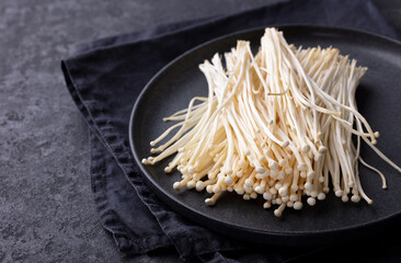 Enoki mushrooms on a black plate. Asian cuisine. Dark background. Copy space.