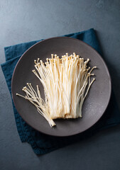Enoki mushrooms on a black plate. Asian cuisine. Dark background. Top view.