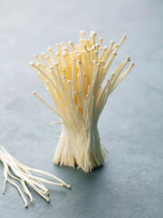 Delicate enoki mushrooms cluster, fresh harvest, minimalist backdrop, culinary inspiration, Asian cuisine touch. Grey background.