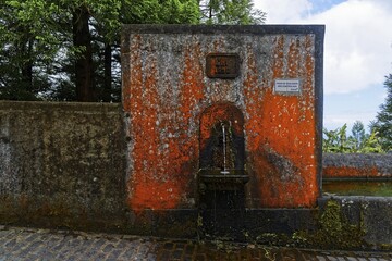 An old stone fountain with moss and algae growth and a weathered historical inscription, crater circular hiking trail, Caldeira das Sete Cidades, Muro das Nove Janelas, Sao Miguel, Portugal