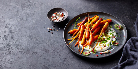 Roasted carrots salad with yogurt. Grey background. Copy space. Close up.