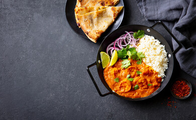 Shrimp curry with fragrant rice, crispy naan, fresh cilantro, lime wedges and aromatic spices. Grey background. Copy space. Top view.