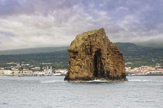 The majestic rock 'Iieu em Pe' rises from the sea, background with Pico Island and the town of Madalena under a cloudy sky, Iieu Deitado, Iieu em Pe, Horta, Faial, Azores, Portugal